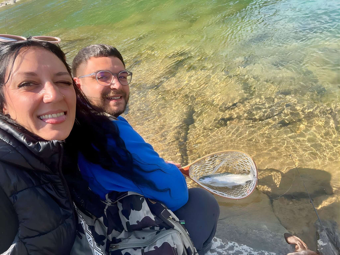 Una coppia sorride mentre utilizza attrezzatura da pesca di qualità in un fiume.